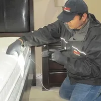 Bed bug inspection technician checking a mattress and bed frame for signs of infestation in Detroit, MI